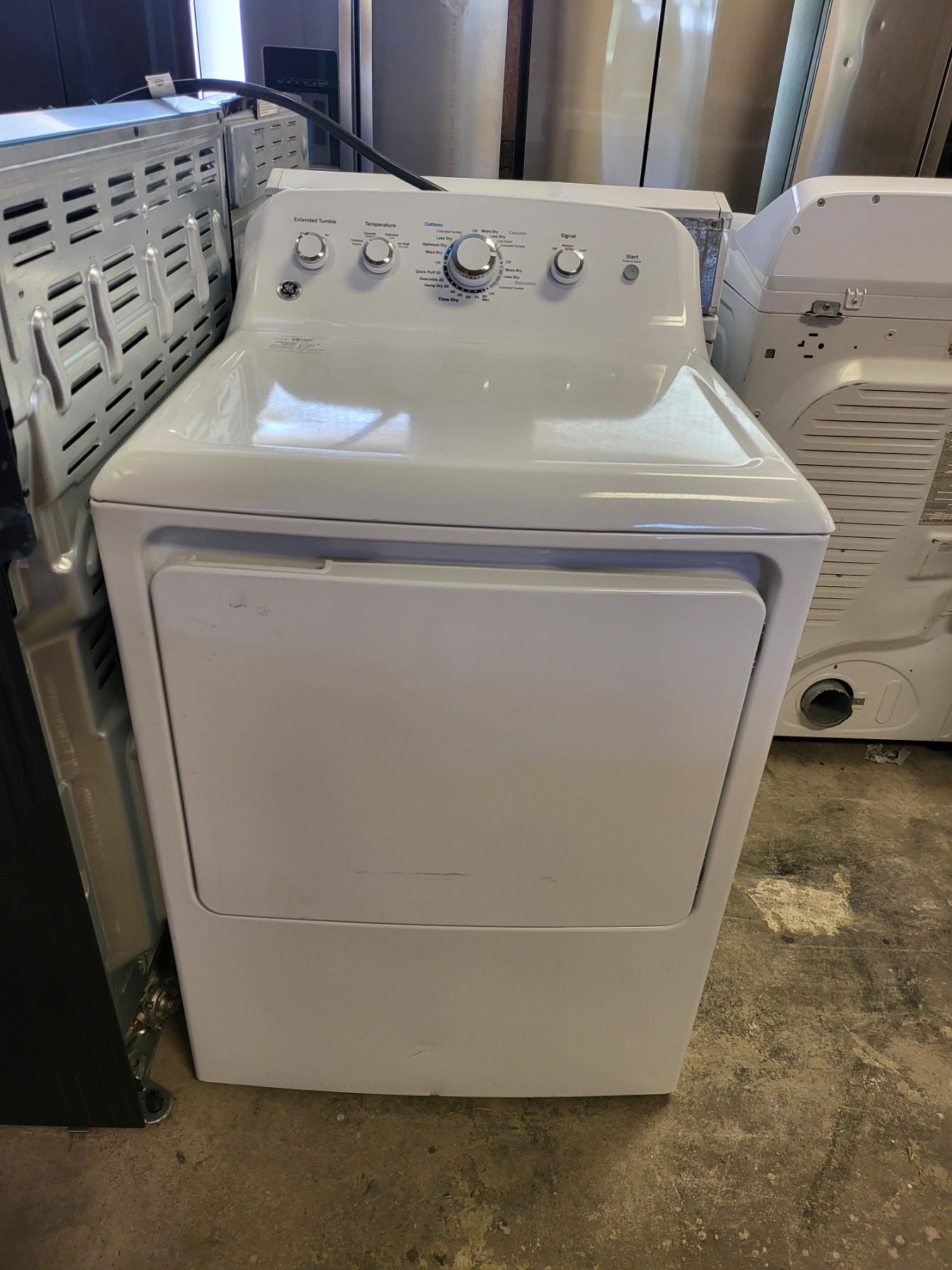 White dryer on a concrete floor with a metal surface in the background